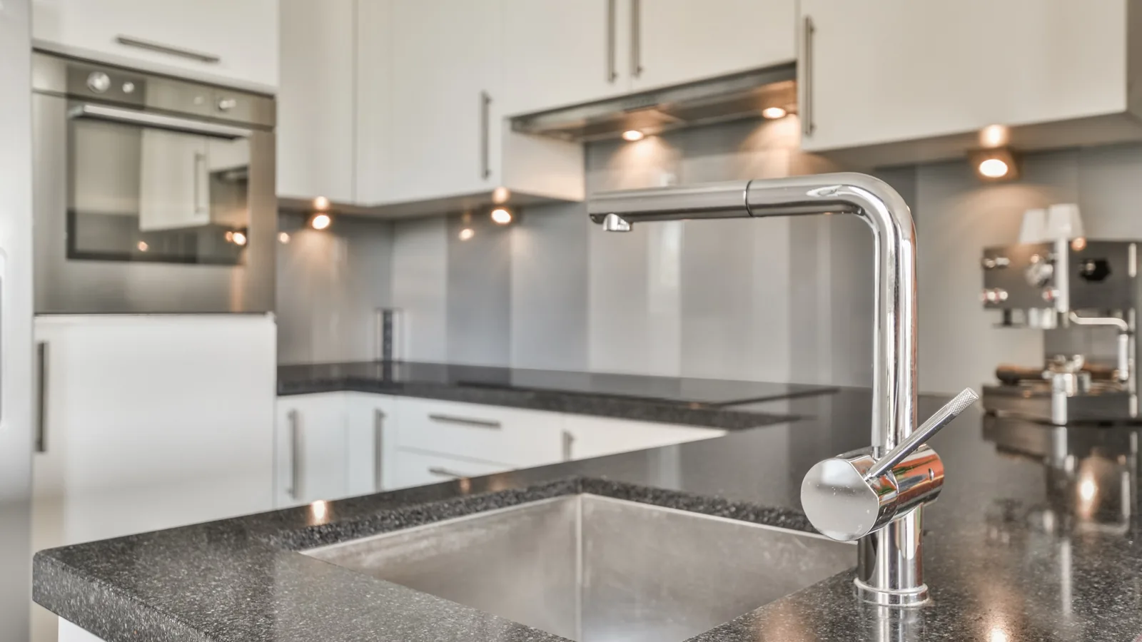 Stainless steel undermount kitchen sink with a chrome pull down faucet on a dark granite countertop