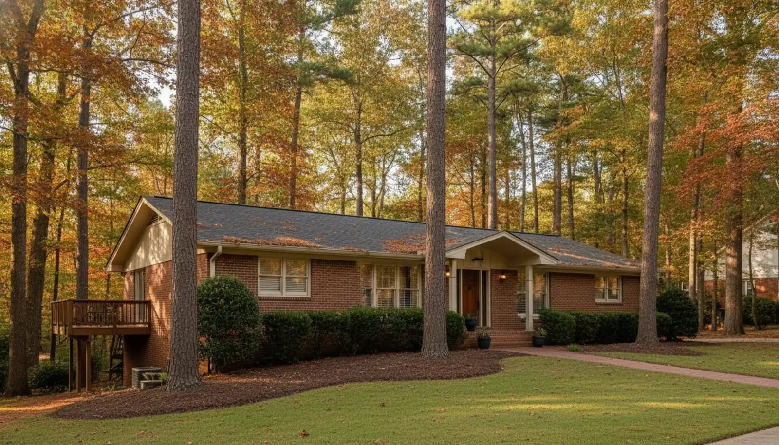 Brick ranch home on a wooded lot in Sandy Springs, Georgia, with tall pines, autumn leaves and a side deck in late afternoon sun