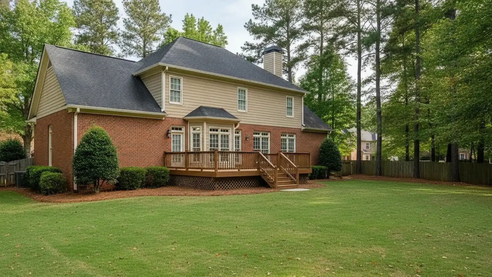 Back of a two story brick and siding home in a Woodstock, Georgia subdivision with a wooden deck, green lawn and tall pine trees