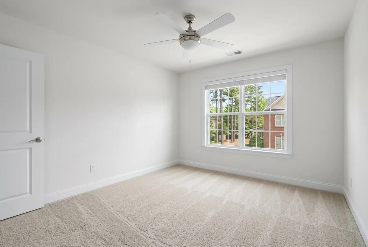 Empty rental bedroom with fresh white paint, new carpet and a ceiling fan, ready for the next tenant