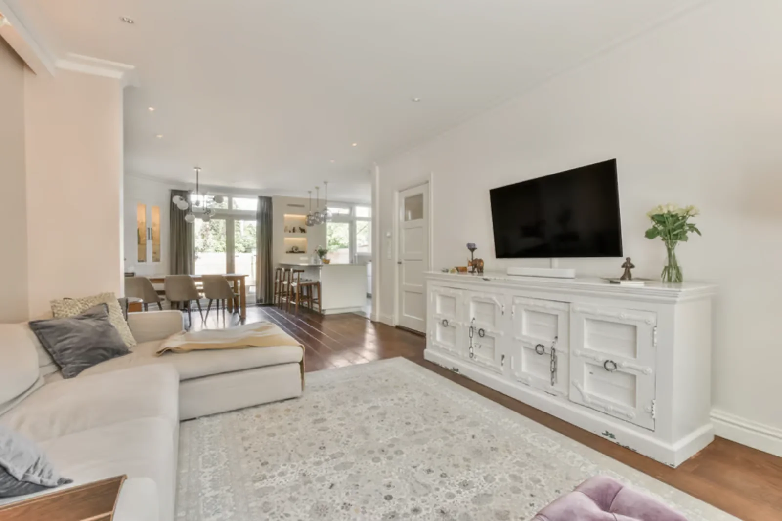 Flat screen TV mounted on a white living room wall above a white media console